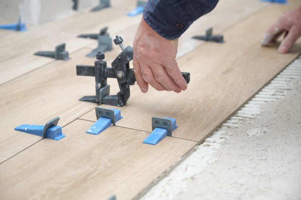 Mason hands adjusting tile levelers between ceramic wood effect tiles.