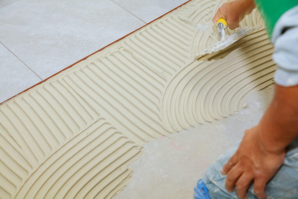 floor tiler Spreading wet mortar before applying tiles on bathroom floor.