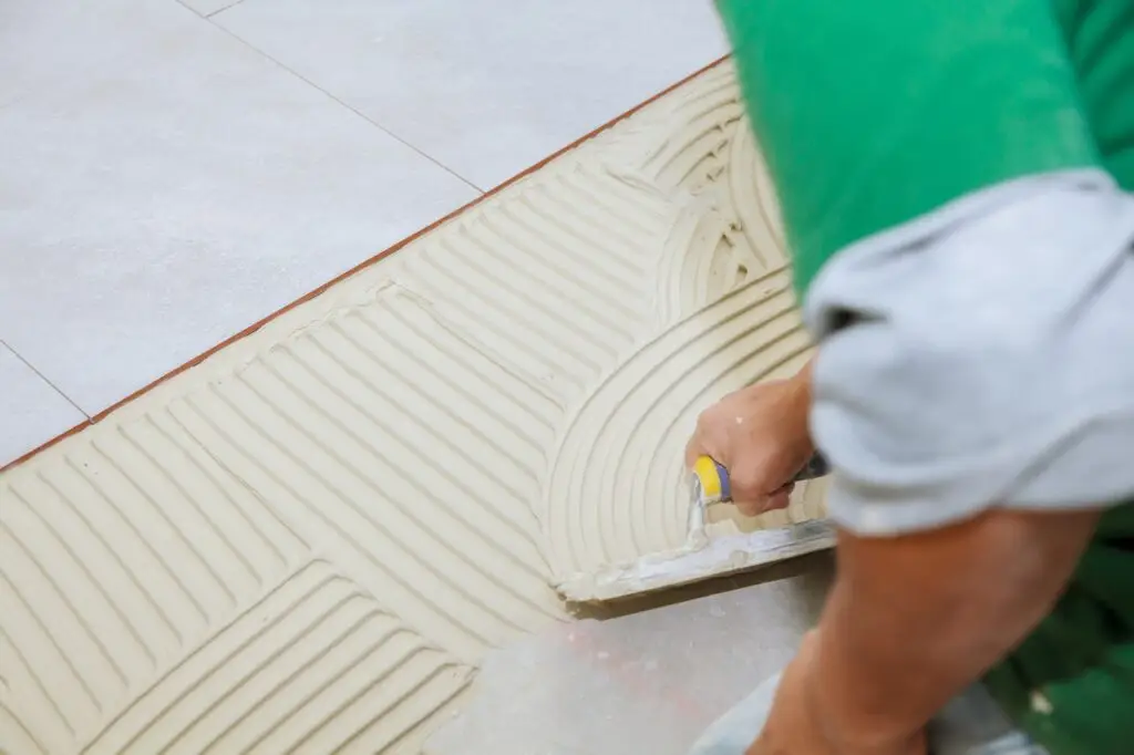 Worker installs tiles on the floor. He put glue using comb trowel. Master puts adhesive